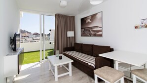 A modern living room with a sofa, a dining table, and a TV. - Apartamentos Los Mocanes (Mogan)