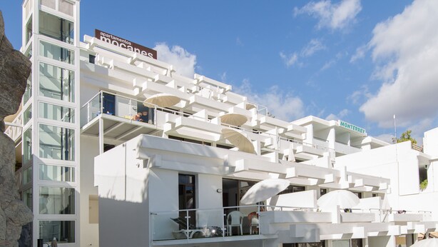 A modern hotel with a swimming pool, white balconies, and outdoor seating areas. - Apartamentos Los Mocanes (Mogan)