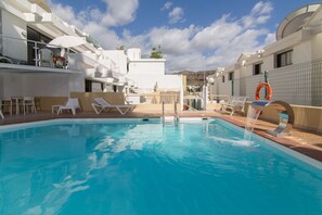 A swimming pool with lounge chairs and a lifebuoy, surrounded by white buildings with balconies.