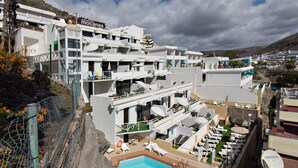 A modern hotel with multiple balconies, a swimming pool, and outdoor seating areas. - Apartamentos Los Mocanes (Mogan)