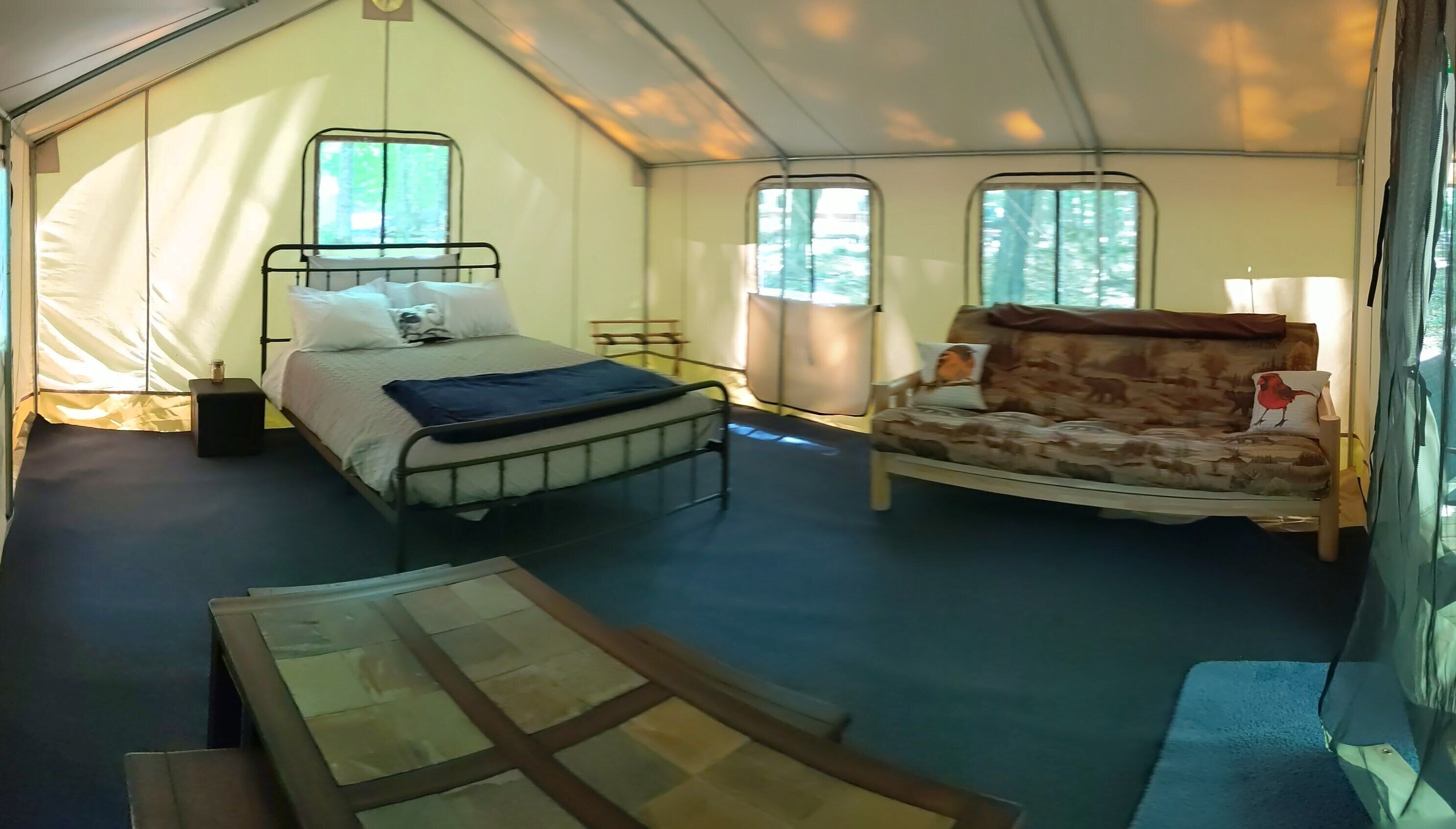 A tented accommodation with a bed, a sofa, and a table.
