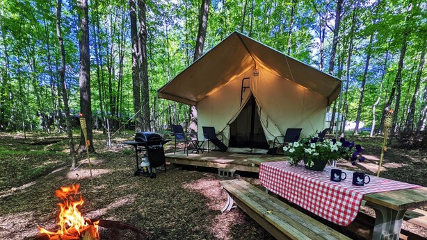 Et teltområde til camping med bålsted, picnicbord og udendørs siddepladser.