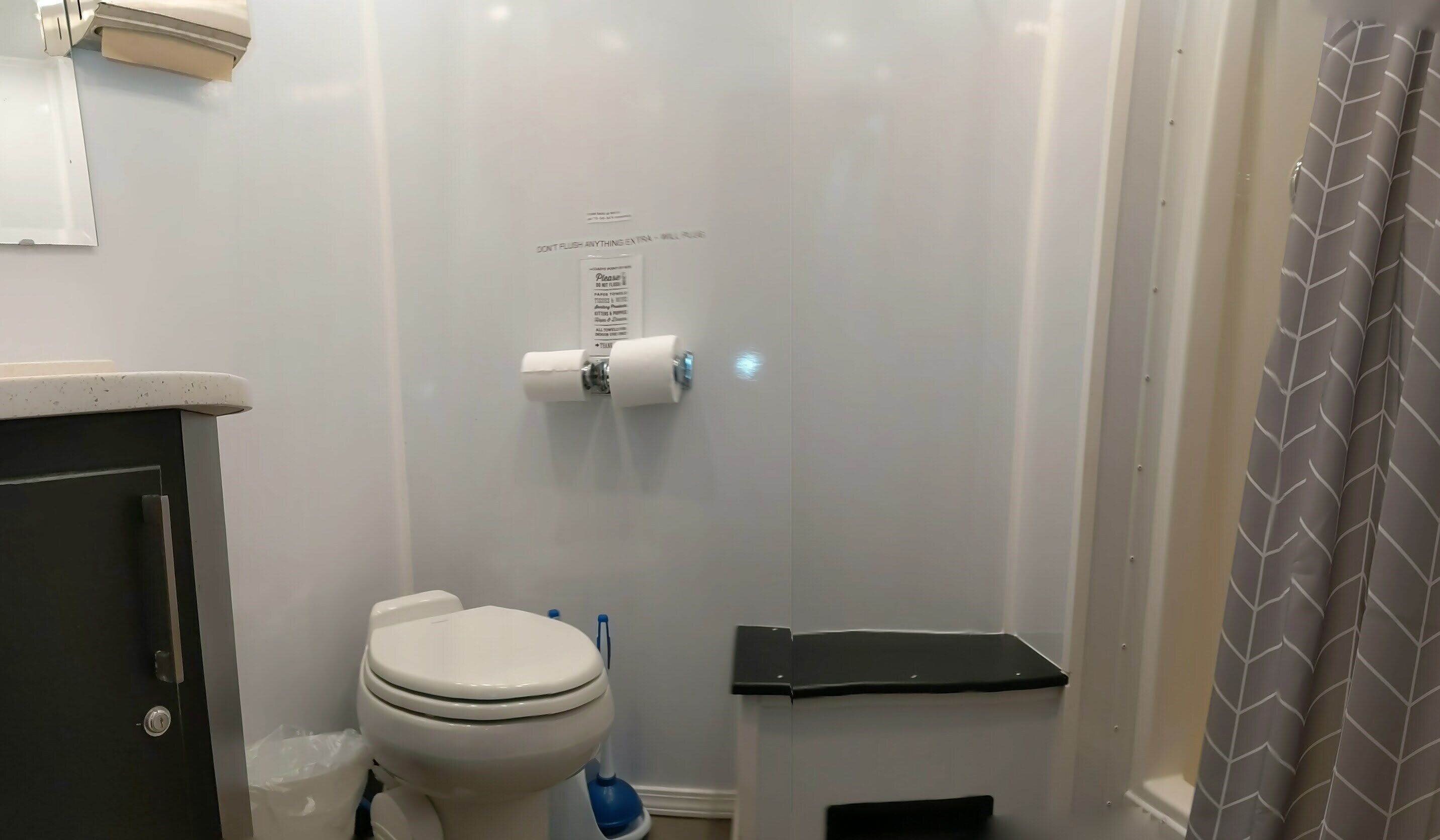A bathroom with a toilet, a paper towel dispenser, and a shower curtain.