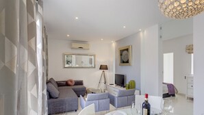 Un salon moderne avec un canapé gris, un téléviseur et un coin repas avec une table dressée pour deux personnes.