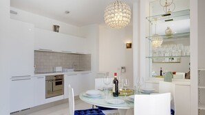Une cuisine moderne avec des meubles blancs, un four encastré et une table à manger en verre, mise avec des assiettes et des verres à vin.