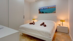 Ein modernes Schlafzimmer mit einem großen Bett, zwei Nachttischlampen und einem Gemälde einer Küstenlandschaft.