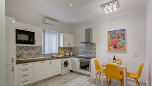 A modern kitchen with a microwave, washing machine, and oven. There is a dining area with yellow chairs and a table. - Cozy Apartment in an Amazing Location (Sliema)