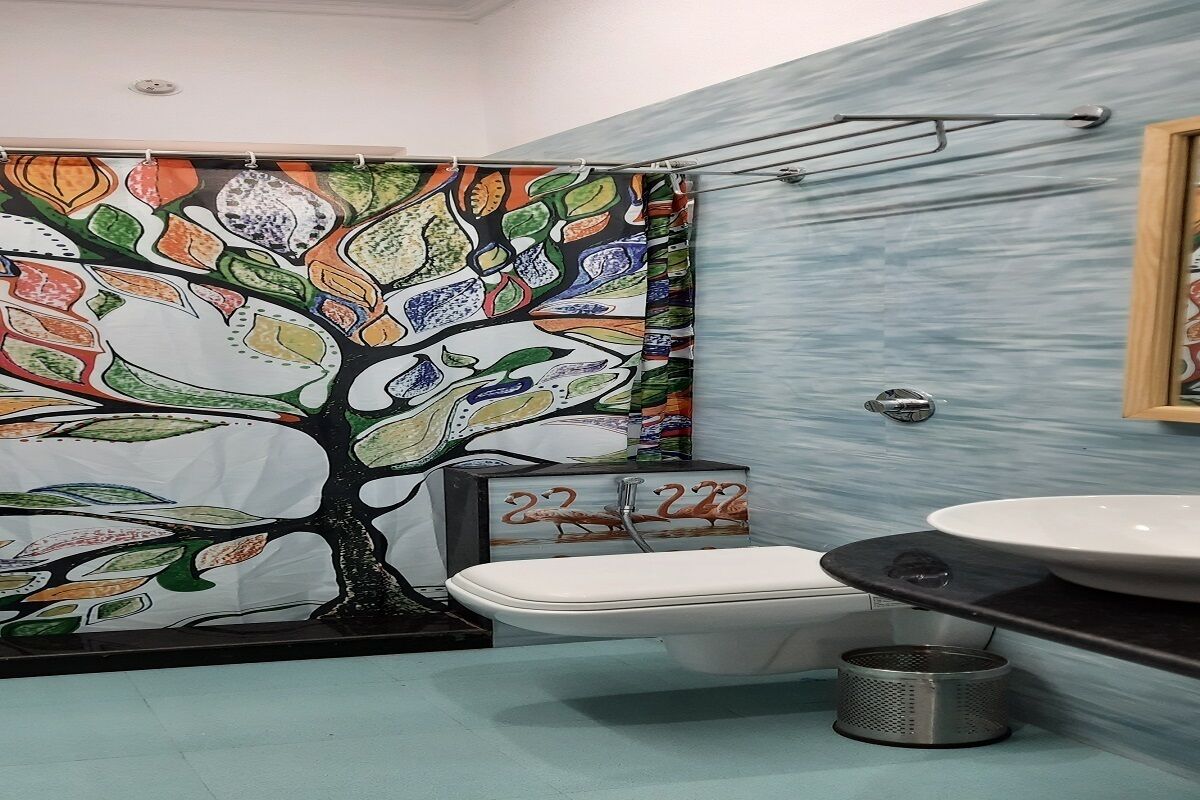 Un baño con un mural de un árbol colorido, un inodoro blanco, un lavabo y una cortina de ducha.