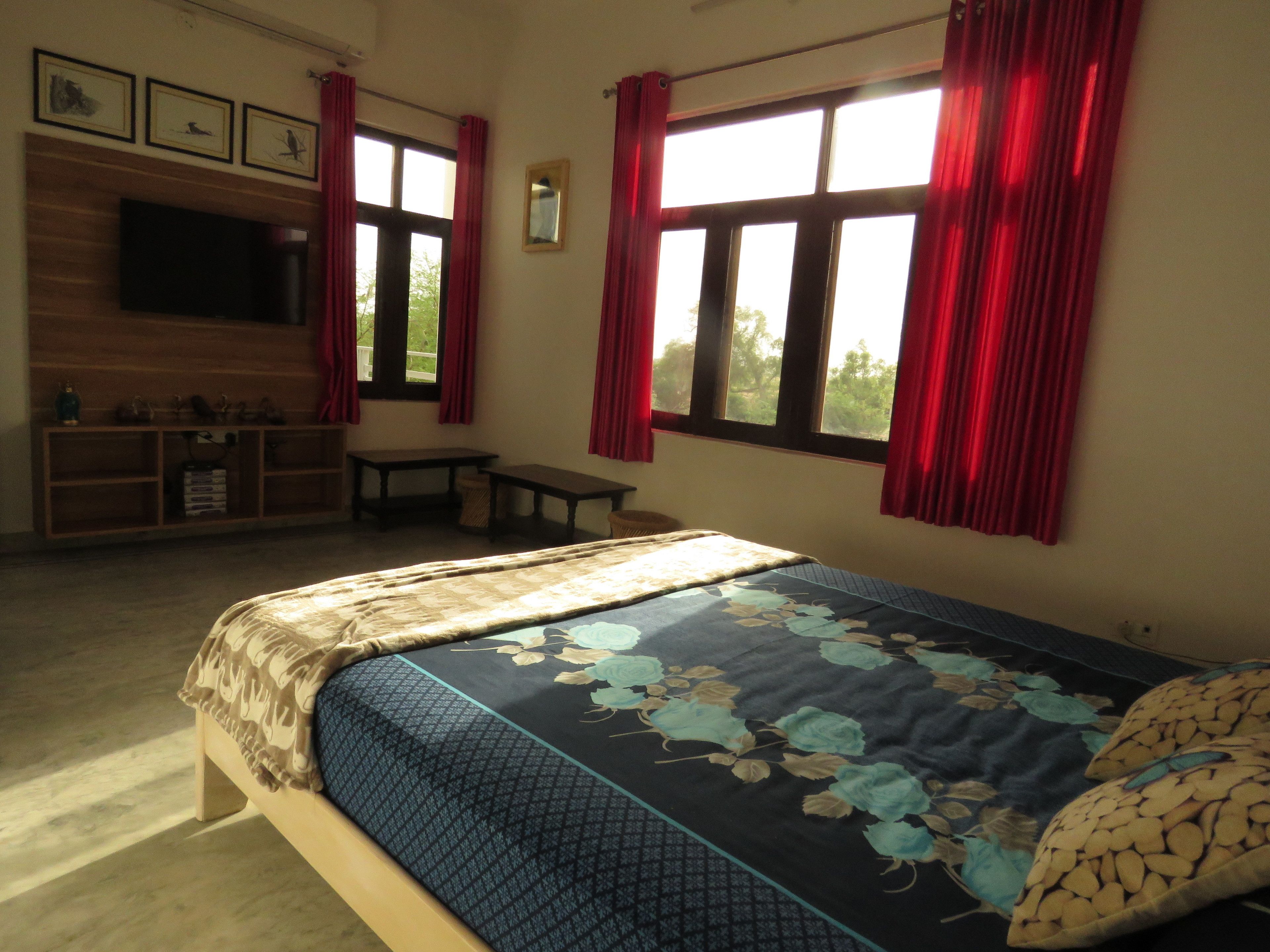A bedroom with a bed, a TV mounted on the wall, a small table, and a window with red curtains.