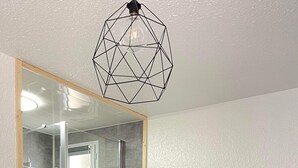 A modern bedroom with a bed, a geometric pendant light, a glass shower enclosure, and a white wall. - Apartment at the foot of the slopes and ideally located in the resort center (Mont-de-Lans)