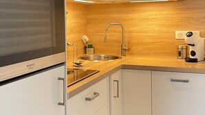 A modern kitchen with white cabinetry, a built-in oven, a microwave, a stainless steel sink, and a wooden backsplash. - Apartment at the foot of the slopes and ideally located in the resort center (Mont-de-Lans)