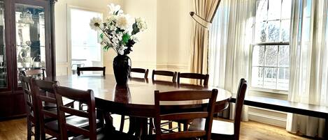 A dining room with a round wooden table, six chairs, and a vase with white flowers.