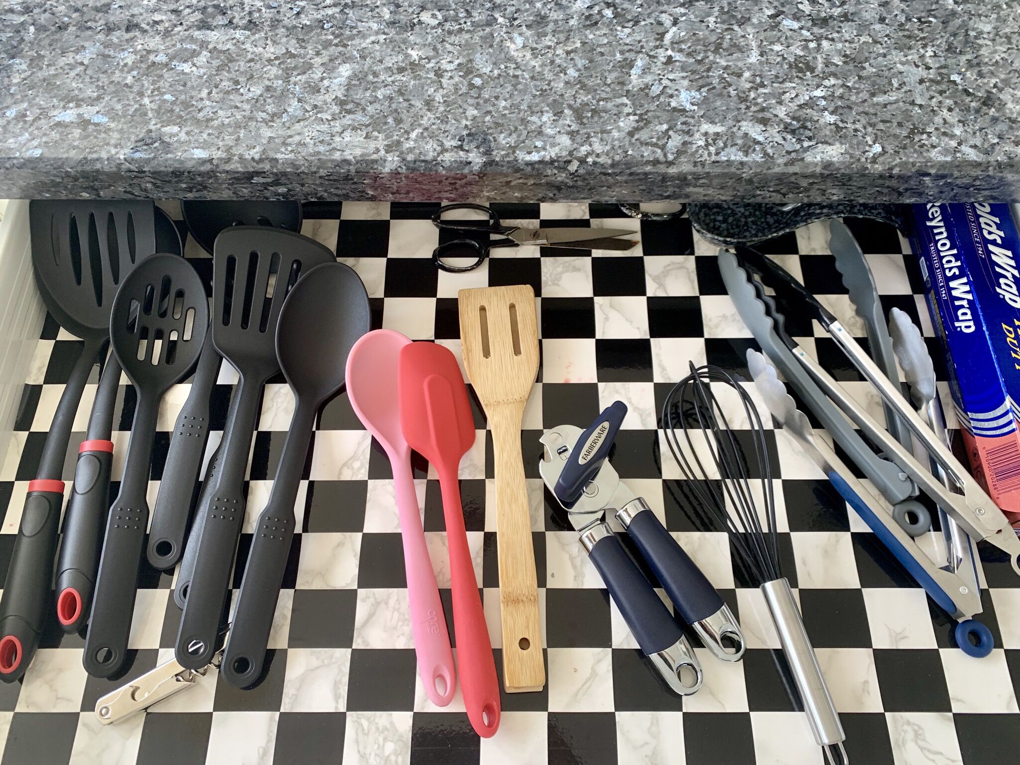 A kitchen counter with various utensils and kitchenware, including spatulas, a wooden spatula, a can opener, and a whisk.