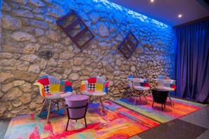Una habitación con pared de piedra, sillas coloridas y una alfombra vibrante.