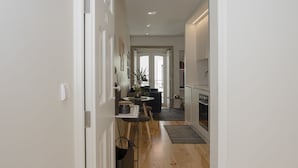 A hallway with wooden flooring, a dining area with a table and chairs, and a kitchen with cabinets and a stove. - Liiiving in Porto - Cozy & Chic Downtown (Porto)