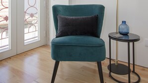 A teal armchair with a dark cushion in a room with wooden flooring, a tall floor lamp, and a small table with a blue vase. - Liiiving in Porto - Cozy & Chic Downtown (Porto)