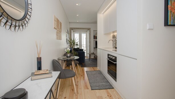 A modern kitchen with a dining area, wooden flooring, and a small round table with chairs. - Liiiving in Porto - Cozy & Chic Downtown (Porto)