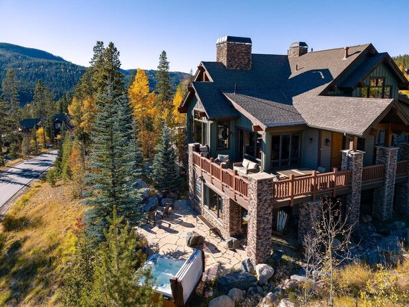 Un grand chalet à plusieurs étages, avec une façade en pierre, un balcon et un jacuzzi dans le jardin.