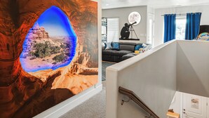 Un salon avec une grande fresque murale, un télescope et un canapé avec des coussins.