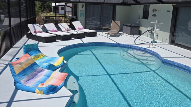 A covered swimming pool area with lounge chairs and a poolside table. - 3 Miles from Beach! Beautiful Canal Home, 3 Bed/3 Bath, heated pool and spa (Englewood)
