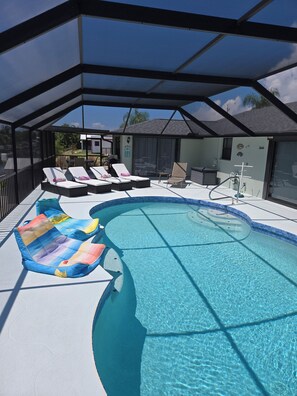 A covered swimming pool area with lounge chairs and a poolside table. - 3 Miles from Beach! Beautiful Canal Home, 3 Bed/3 Bath, heated pool and spa (Englewood)