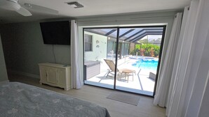 A bedroom with a bed, a TV, a ceiling fan, and a view of an outdoor swimming pool through a sliding glass door. - 3 Miles from Beach! Beautiful Canal Home, 3 Bed/3 Bath, heated pool and spa (Englewood)