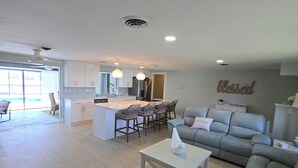 A spacious living area with a kitchen, a dining area with bar stools, and a grey sofa. - 3 Miles from Beach! Beautiful Canal Home, 3 Bed/3 Bath, heated pool and spa (Englewood)