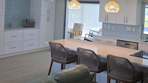 A modern kitchen with white cabinets, a central island with bar stools, and pendant lighting. - 3 Miles from Beach! Beautiful Canal Home, 3 Bed/3 Bath, heated pool and spa (Englewood)