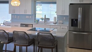 A modern kitchen with a central island, bar stools, stainless steel appliances, and a view to the outside. - 3 Miles from Beach! Beautiful Canal Home, 3 Bed/3 Bath, heated pool and spa (Englewood)