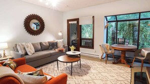 Ein Wohnzimmer mit Sofa, Couchtisch, Esstisch mit Stühlen, einem großen Fenster und einem dekorativen Spiegel.