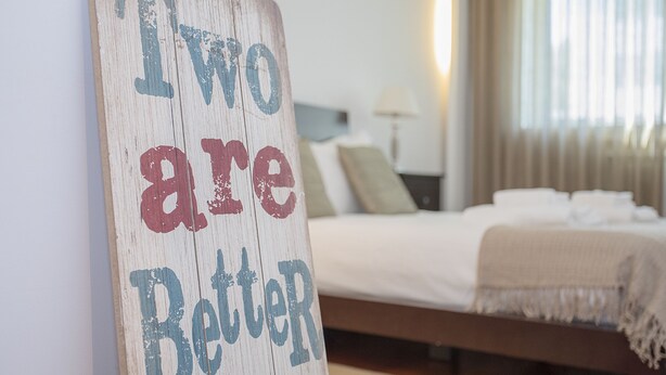 Una camera da letto con un letto, cuscini e un cartello con la scritta 'Two are Better'.