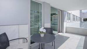 Un'area salotto esterna moderna con un tavolo rotondo e due sedie, una pianta in vaso e una porta vetrata che dà su un balcone.