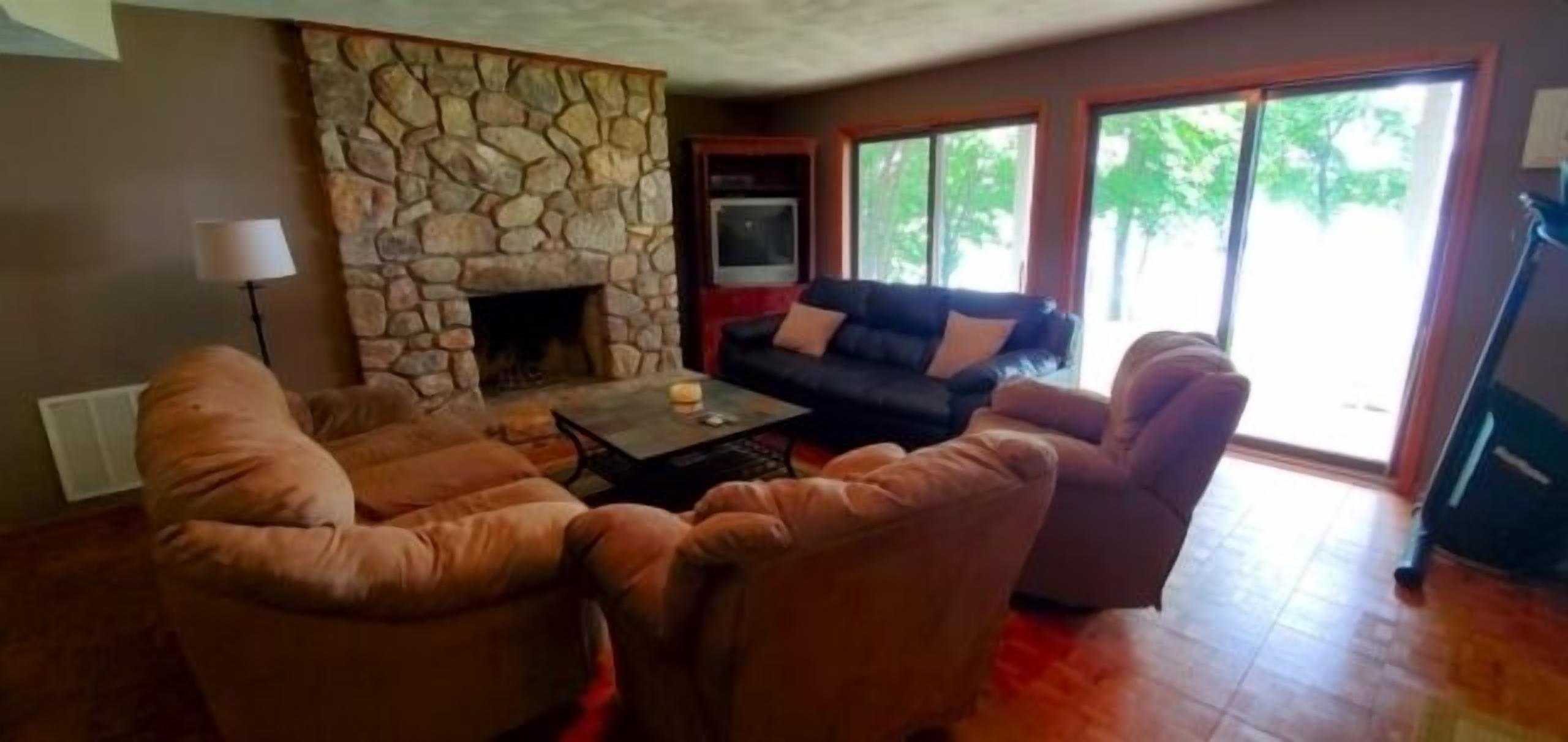 A living room with a stone fireplace, leather sofas, and a large window with a view of trees.