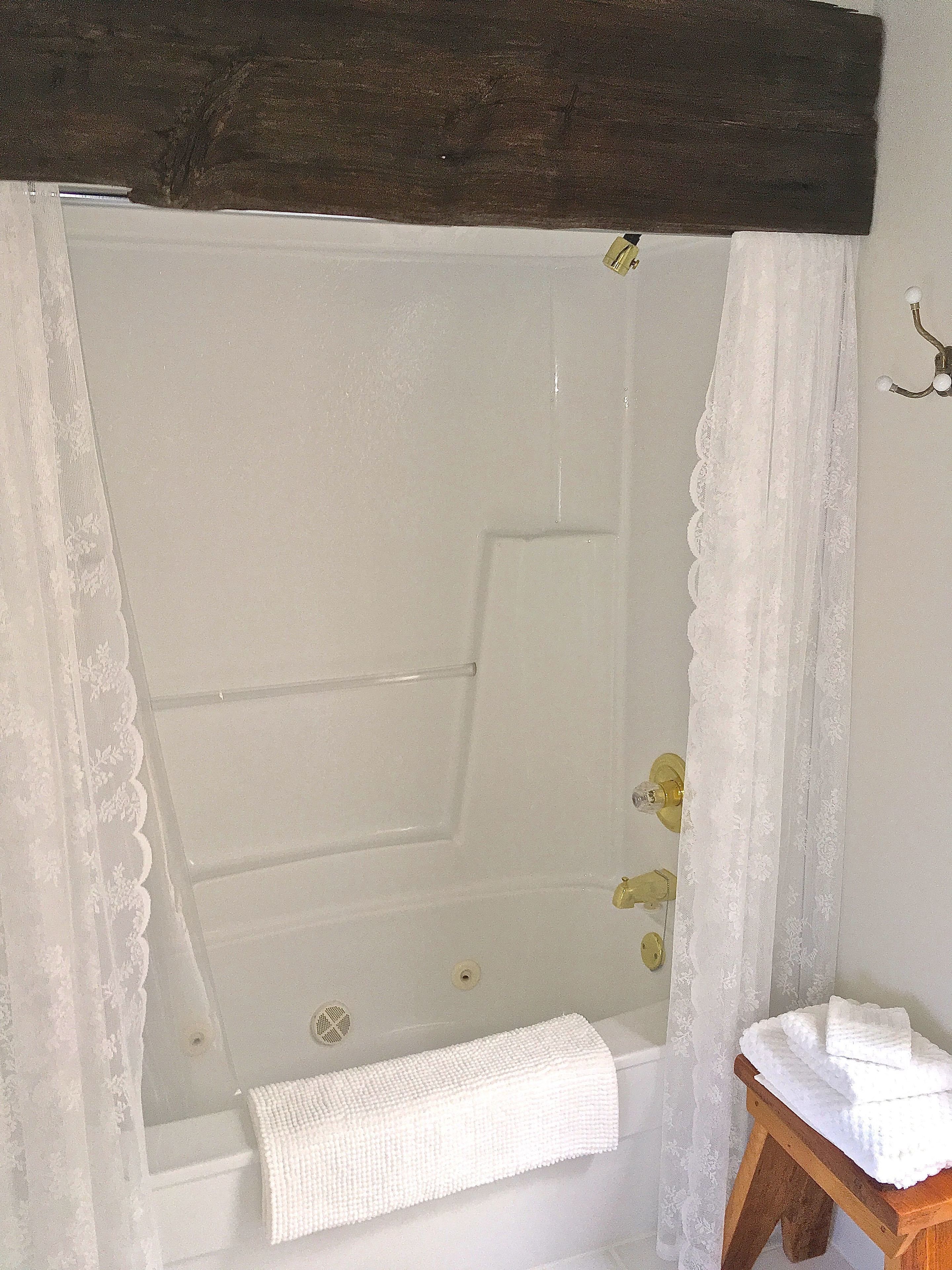 A bathroom with a bathtub, a wooden stool with towels, and a white towel on the floor.