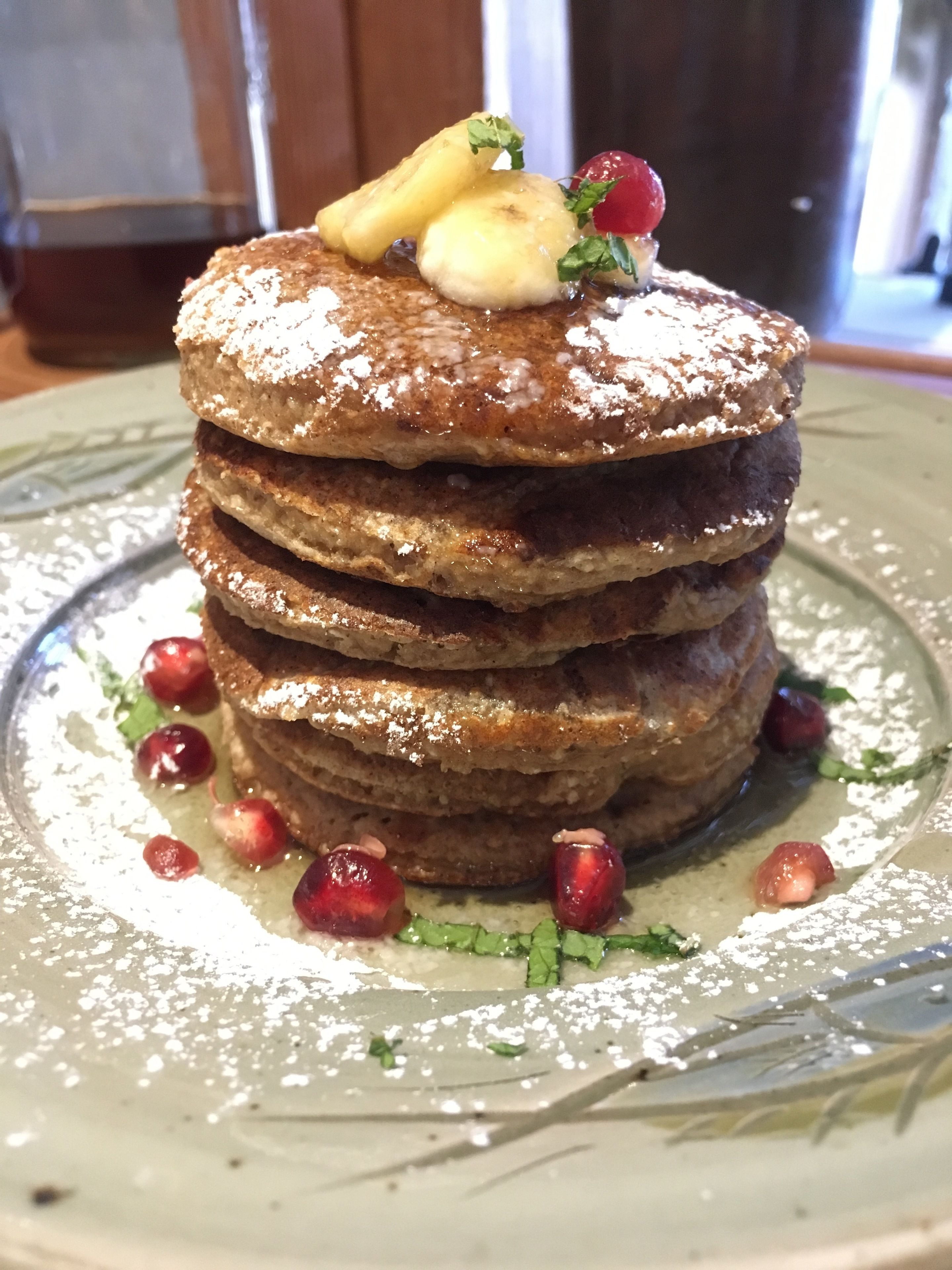 Una pila de panqueques con fruta y azúcar glas sobre un plato.