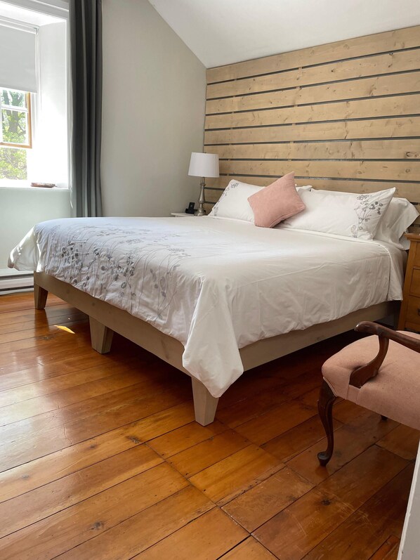 Un dormitorio con una cama de madera, una mesita de noche con lámpara, una silla y una ventana con cortinas.