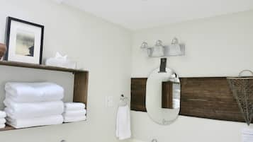 Un baño con un estante de madera que sostiene toallas dobladas, un espejo grande y una lámpara de pared.