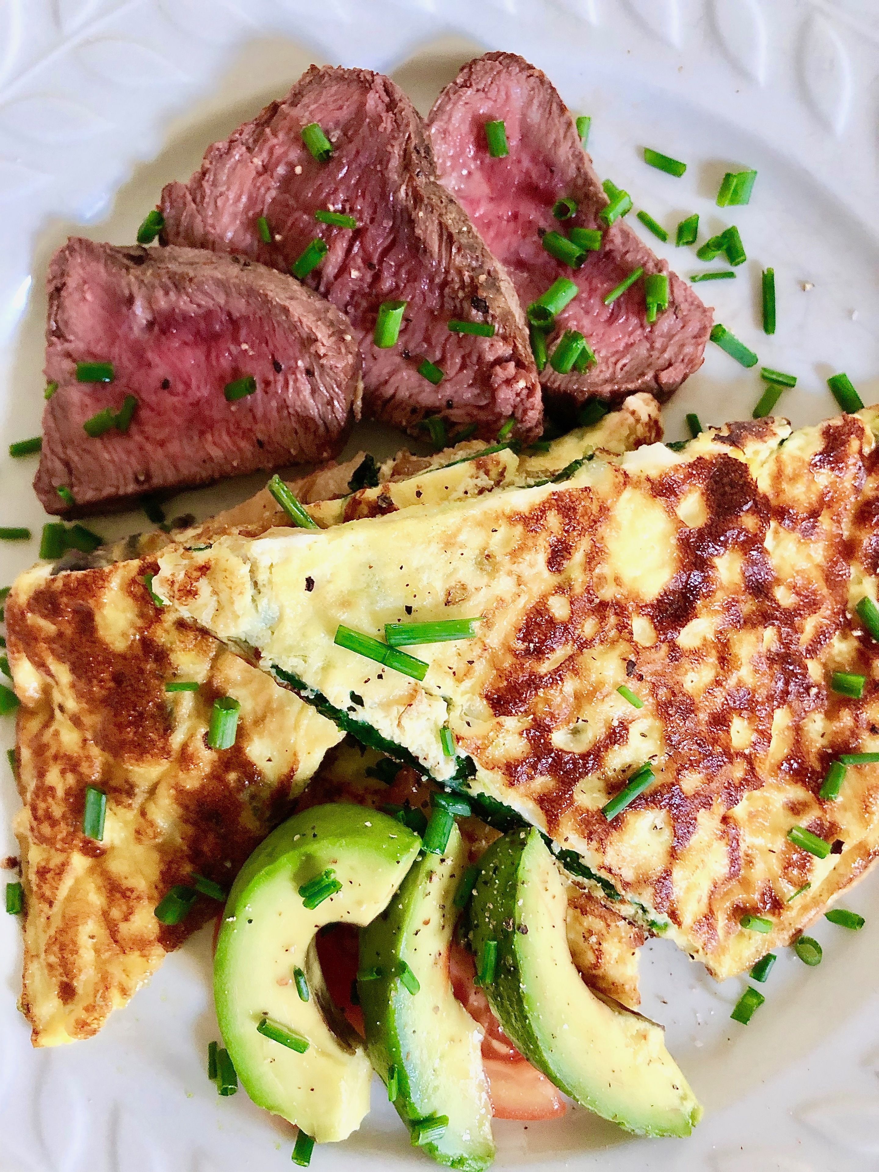A plate with sliced steak, a grilled omelette, and avocado slices.