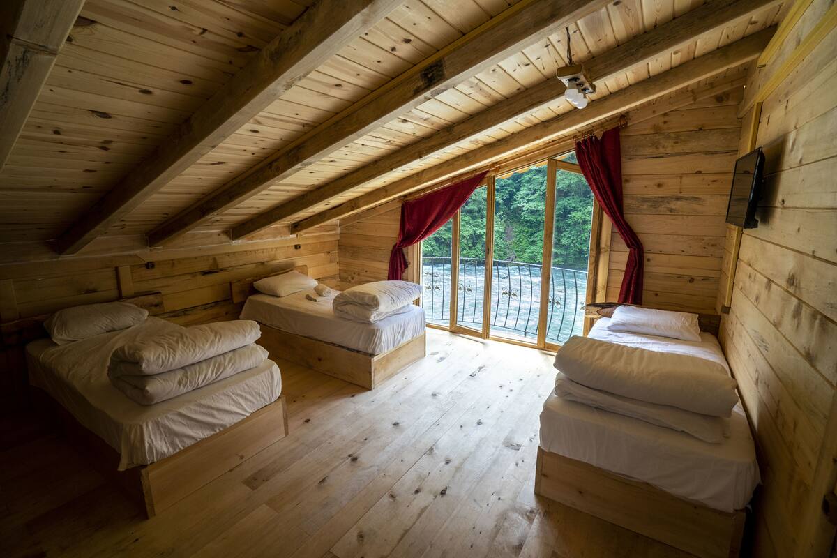 Une cabine avec deux lits en bois, une grande fenêtre ornée de rideaux rouges et un téléviseur fixé au mur.