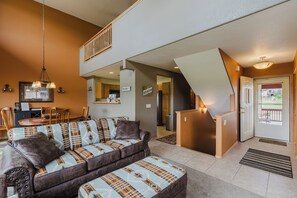Uma sala de estar com sofá, pufê, área de refeições, cozinha e escada.