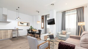 A modern living room with a sofa, armchair, and coffee table. There is a dining area with a table and chairs, and a kitchen area with a counter and cabinets. - A (VA013.2 ) TH Ayuntamiento 2D (Valencia / València)