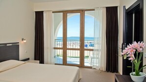 A hotel room with a bed, a nightstand, a potted plant, and a view of the beach through large windows. - Hotel Viand (Sunny Beach)