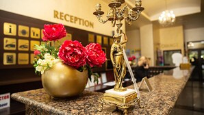 A reception area with a gold candelabra and a vase of red and white flowers on a granite counter. - Hotel Viand (Sunny Beach)