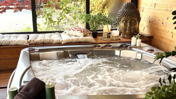 A hot tub with a view of a garden and a Buddha statue.