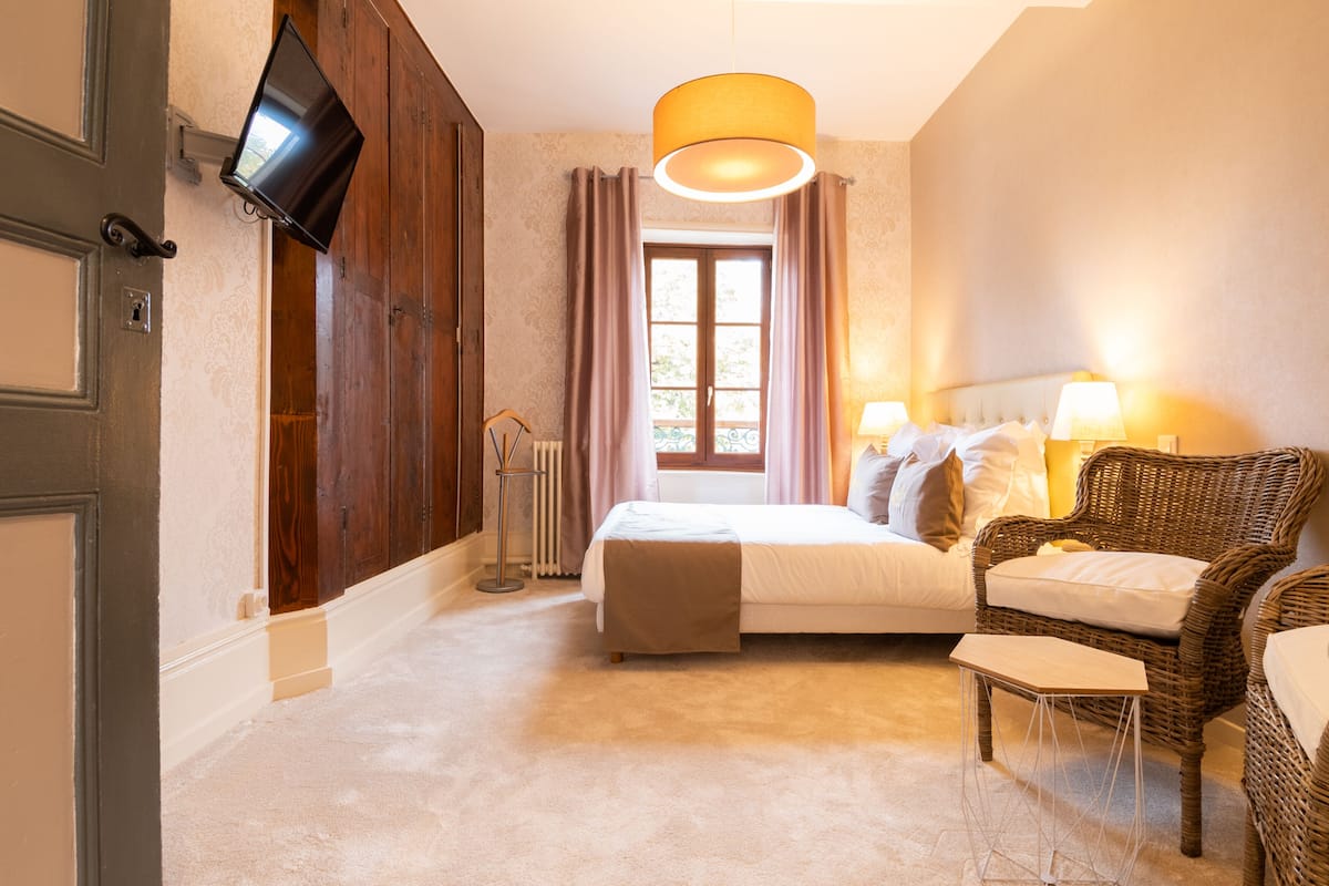Une chambre à coucher avec un lit, une chaise, un téléviseur fixé au mur et une fenêtre avec des rideaux.