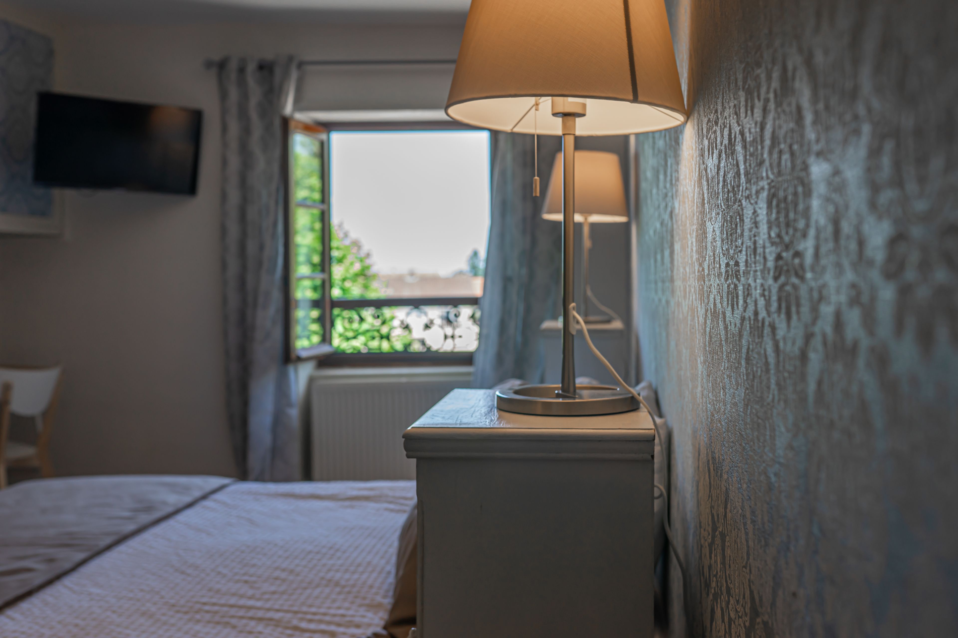 Une chambre d’hôtel avec un lit, une lampe de chevet, un téléviseur fixé au mur et une fenêtre avec des rideaux.