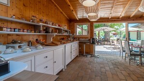 A wooden interior with a kitchen counter, shelves with jars, and a dining area with chairs and umbrellas.