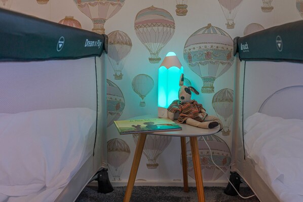 Une chambre avec deux lits, une petite table sur laquelle se trouve un livre, une lampe et un jouet en peluche.