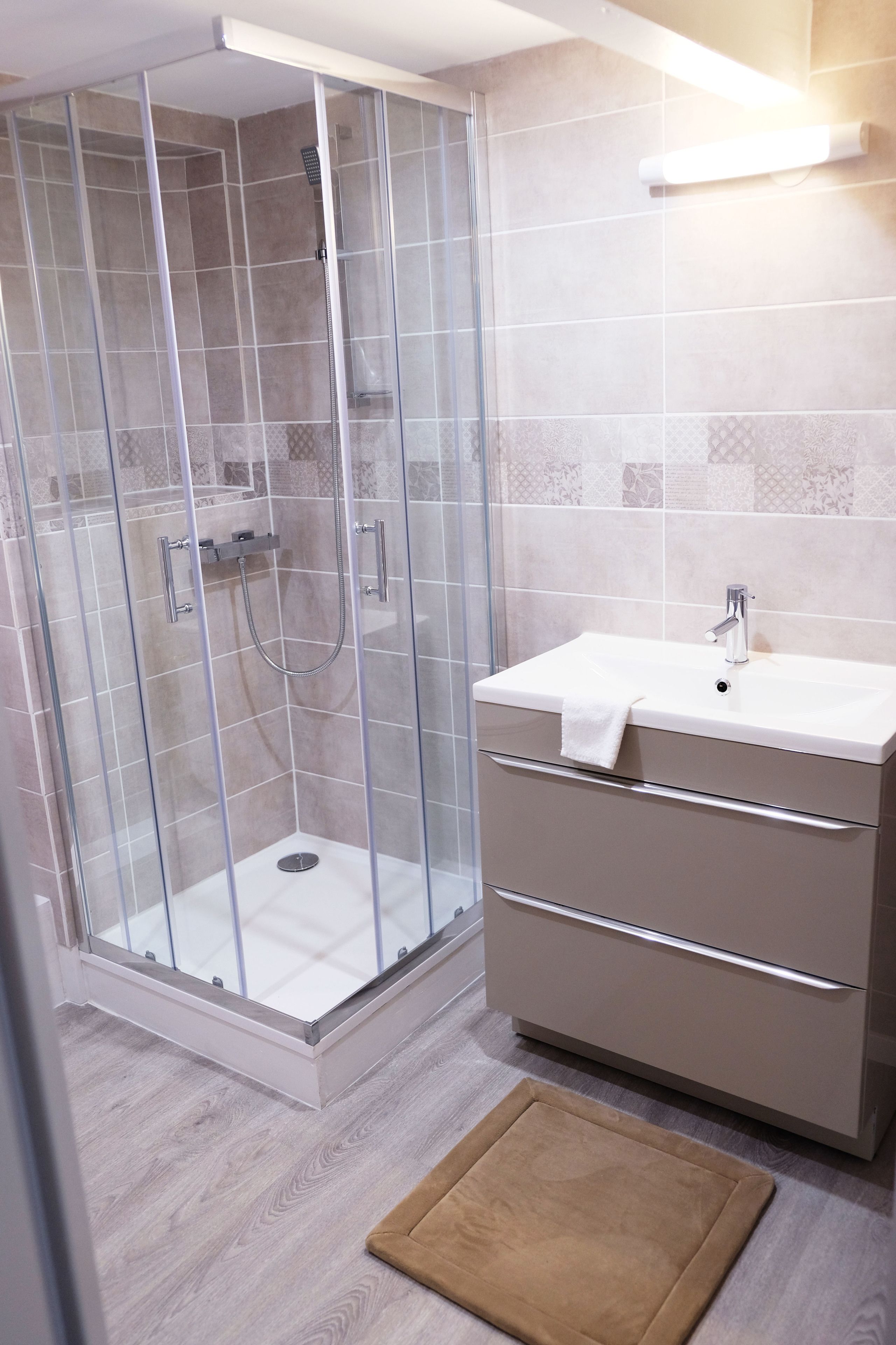 A modern bathroom with a glass-enclosed shower, a white sink, and a beige vanity.