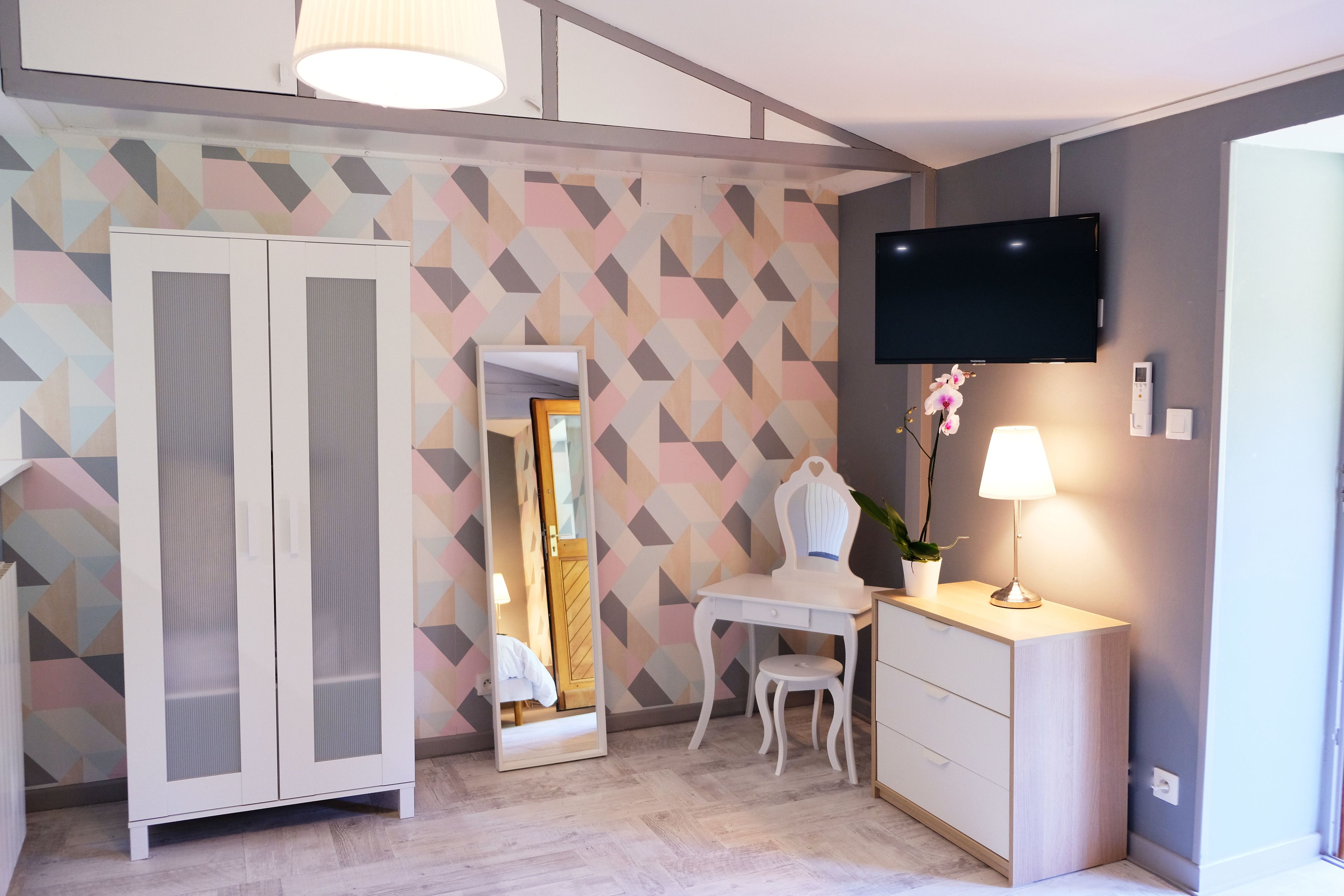 Une chambre moderne équipée d’une armoire, d’un bureau, d’une chaise, d’un téléviseur et d’un miroir.